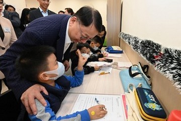 政務司司長兼扶貧委員會主席陳國基今日(十二月十八日)視察深水埗社區客廳,是「社區客廳試行計劃」首個項目。勞工及福利局局長孫玉菡亦有隨行。圖示陳國基(站立,左一)參觀溫習室,與正在做功課的兒童交流。
