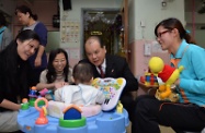 Mr Cheung (second right) plays with a baby while visiting the childcare facilities of the home.