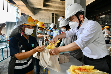 勞工及福利局局長孫玉菡今日（七月十三日）回答立法會議員有關預防僱員工作時中暑的口頭質詢後，午飯時間探訪機場航天城工地，親身瞭解地盤的預防中暑措施，同時為在戶外辛勞工作的工友打氣，提醒他們留意健康，定時補充水分，並到有冷氣或較清涼的地方小休。圖示孫玉菡（右一）派發防中暑物資包給建築地盤工友。